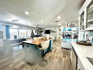 A modern kitchen with a central island, a coffee bar, and a dining area with a view. - TIKI on the CANAL mini-putt pool/spa kayak fishing (Cape Coral)