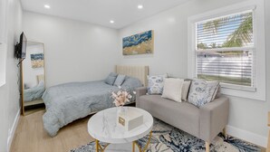 A bedroom with a bed, a sofa, a TV, a ceiling fan, and a painting on the wall. - 3 Miles to Atlantic Ave - The Delray Chic Cottage (Delray Beach)