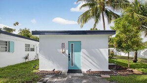 A modern building with a teal door, a small porch, and a number sign above the door. - 3 Miles to Atlantic Ave - The Delray Chic Cottage (Delray Beach)