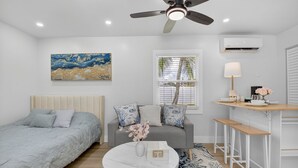 A bedroom with a bed, a sofa, a round table, a ceiling fan, and a window with blinds. - 3 Miles to Atlantic Ave - The Delray Chic Cottage (Delray Beach)