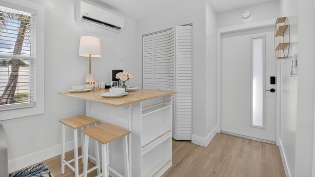 A compact kitchen with a wooden countertop, white bar stools, a wall-mounted air conditioner, and a door with a white closet. - 3 Miles to Atlantic Ave - The Delray Chic Cottage (Delray Beach)