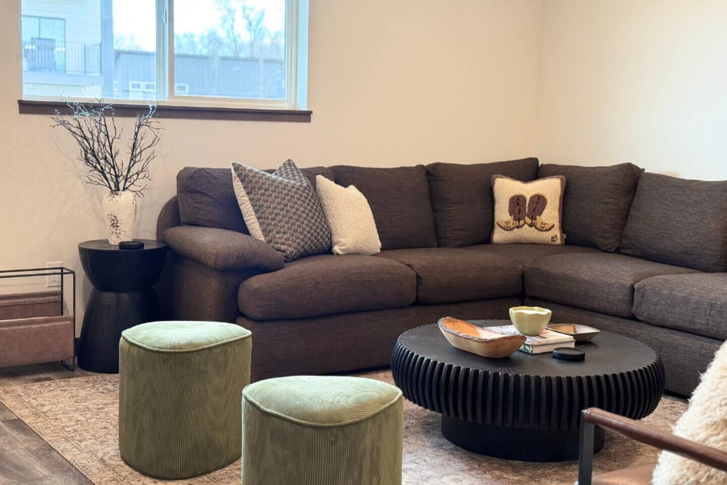 A modern living room with a sectional sofa, two ottomans, a round coffee table, and a vase with branches.