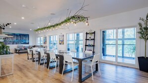 A spacious dining area with a long table, white chairs, and a ceiling light fixture with hanging branches. - *NEW* Stunning Waterfront Mansion | Hot Tub | Falls (St. Catharines)