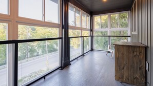 A spacious balcony with large windows, a wooden cabinet, and a chair. - *NEW* Stunning Waterfront Mansion | Hot Tub | Falls (St. Catharines)