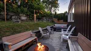 A wooden deck with a fire pit, outdoor seating, and string lights. - *NEW* Stunning Waterfront Mansion | Hot Tub | Falls (St. Catharines)