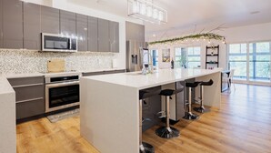 A modern kitchen with a central island, stainless steel appliances, and a bar area. - *NEW* Stunning Waterfront Mansion | Hot Tub | Falls (St. Catharines)