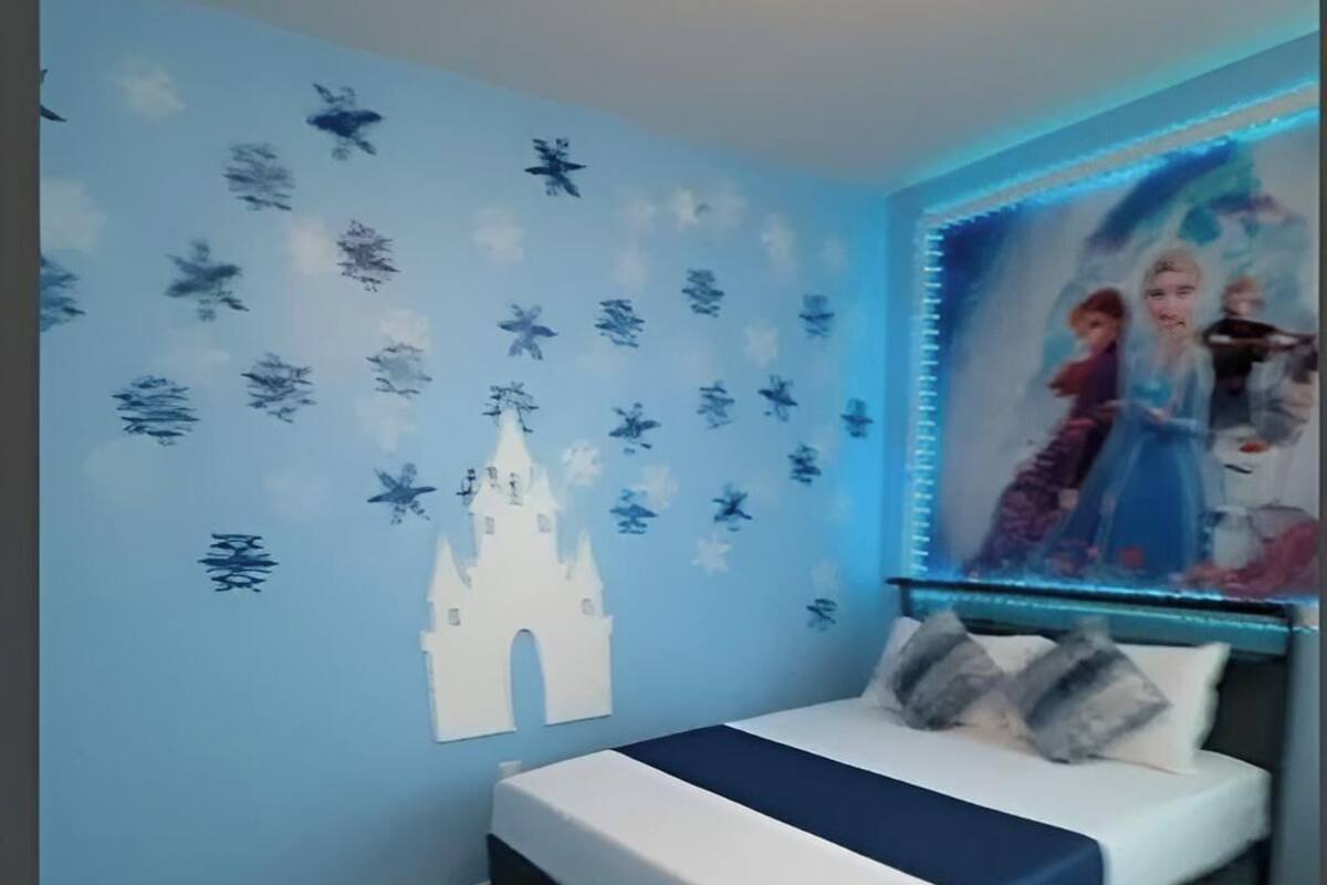 A bedroom with a bed, a wall with a castle and snowflake decals, and a poster of animated characters.