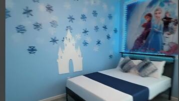 A bedroom with a bed, a wall with a castle and snowflake decals, and a poster of animated characters.