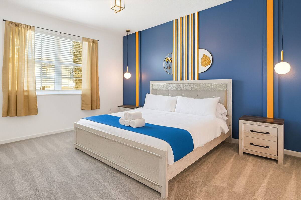 A hotel room with a bed, a nightstand, a wall with vertical stripes, and a window with curtains.