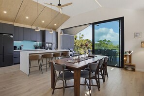 A modern kitchen with a central island, bar stools, and a dining area with a large table and chairs. - Panorama Lookout | Brand New Spacious Winter Retreat with Ocean Views (Normanville)