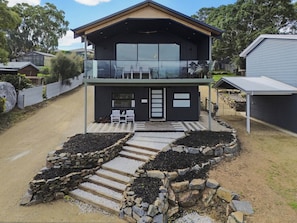 A modern two-story house with a balcony, stone steps, and a small outdoor seating area. - Panorama Lookout | Brand New Spacious Winter Retreat with Ocean Views (Normanville)
