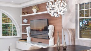 Un intérieur moderne agrémenté d’un grand téléviseur à écran plat, de bustes décoratifs et d’un lustre original.
