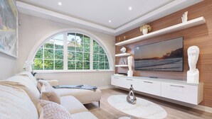 Un salon moderne doté d’une fenêtre incurvée, d’un téléviseur à écran plat, d’un canapé blanc et d’une table basse en marbre.
