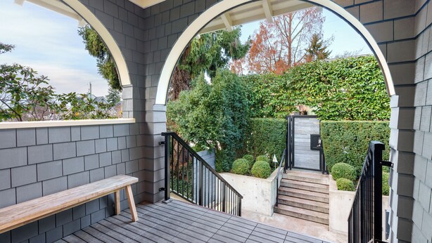 Un espace extérieur abrité, doté d’un banc en bois, d’un escalier et offrant une vue sur un jardin.