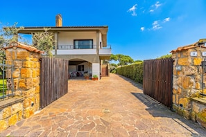 A two-story house with a stone facade, a balcony, and a paved driveway leading to the entrance.