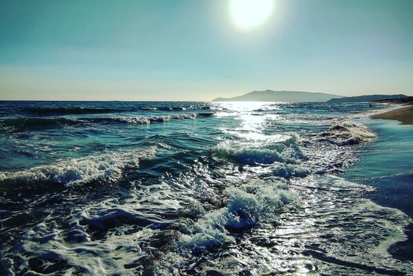Ein Strand mit Wellen, einem klaren Himmel und Bergen in der Ferne.