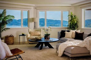 A cozy living room with a view of mountains, a comfortable sofa, a chair, and a coffee table with a book and flowers. - Luxury Tiburon Retreat • Golden Gate Bridge / Bay Views from All 5 King Bedrooms (Tiburon)