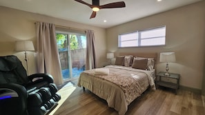 Un dormitorio con cama, sillón de masaje, ventilador de techo y ventana con persianas.