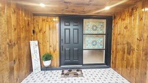 Una puerta de madera con marco negro, un felpudo, una planta en maceta y un cartel que dice 'SPRING'.