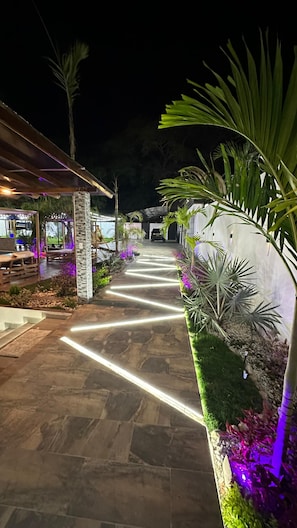A pathway leading to a building with a covered seating area and a stone-paved entrance.