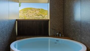 A modern bathroom with a large bathtub, a wooden vanity, and a view of a hilly landscape.