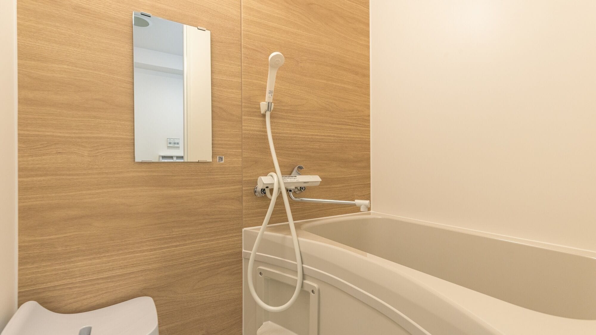 A bathroom with a wooden wall, a white bathtub, a handheld showerhead, and a mirror.