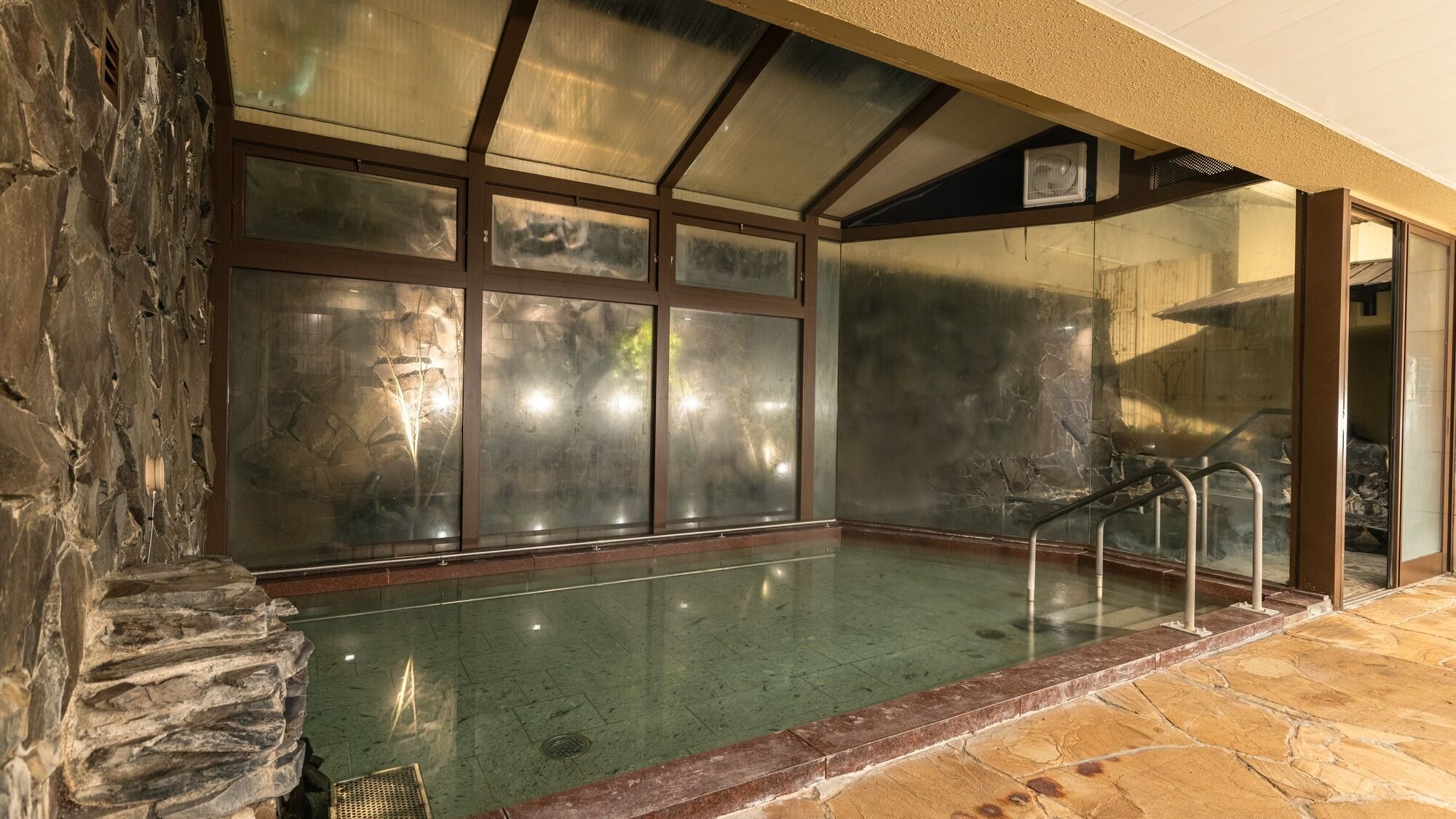 Ein Schwimmbecken mit Steinwänden und einer Glaskonstruktion, einer Metalltreppe und einem Steinboden.