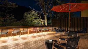 Une terrasse extérieure avec un plancher en bois, plusieurs chaises, une table et un parasol.