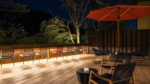 An outdoor deck with wooden flooring, a series of chairs, a table, and an umbrella. - HOTEL nehako (Hakone)