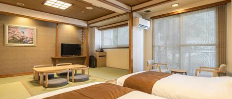 Ein Hotelzimmer mit Tatami-Matten, einem Fernseher, einem Schreibtisch und einem Bett.