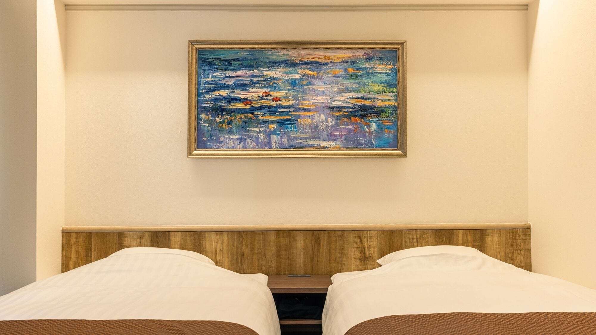 Una habitación de hotel con una cama, una mesita de noche y un cuadro en la pared.