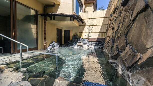 Un espace de bien-être comprenant une source d’eau chaude, des murs en pierre et une terrasse en bois.