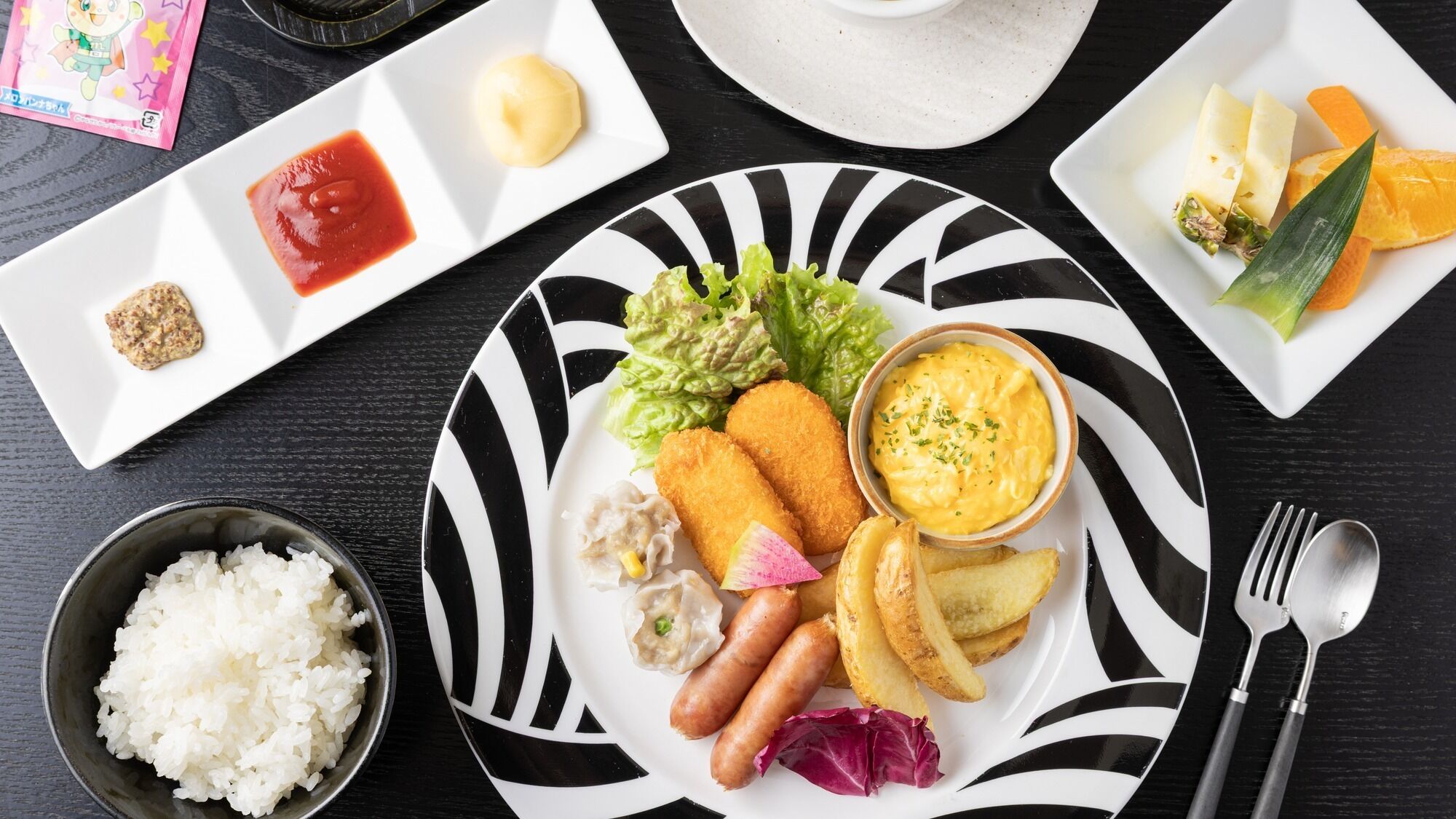 A plate with food items, a bowl of rice, and a spoon.