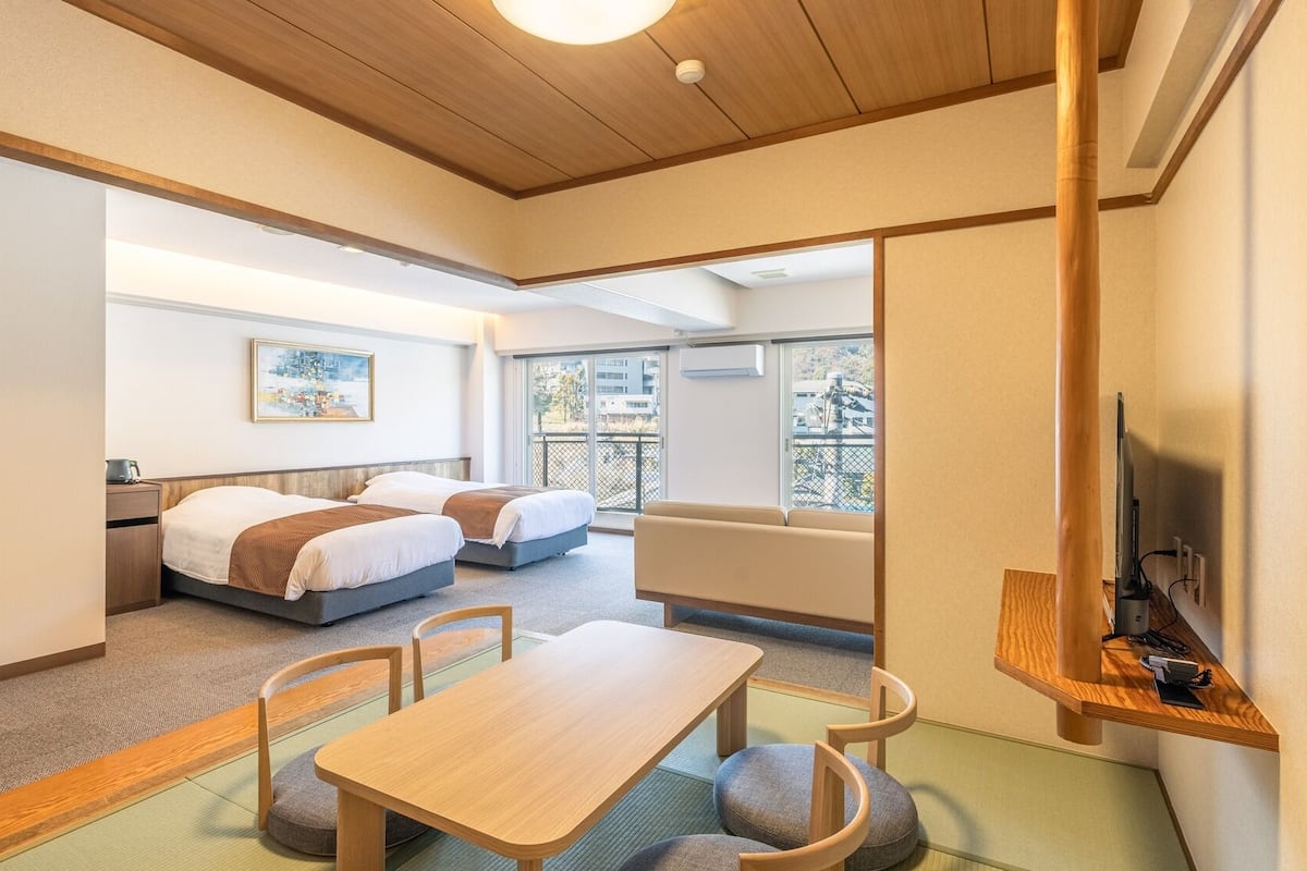 Une chambre d’hôtel avec un plafond en bois, une table à manger avec des chaises, un canapé, deux lits et un téléviseur posé sur un meuble en bois.