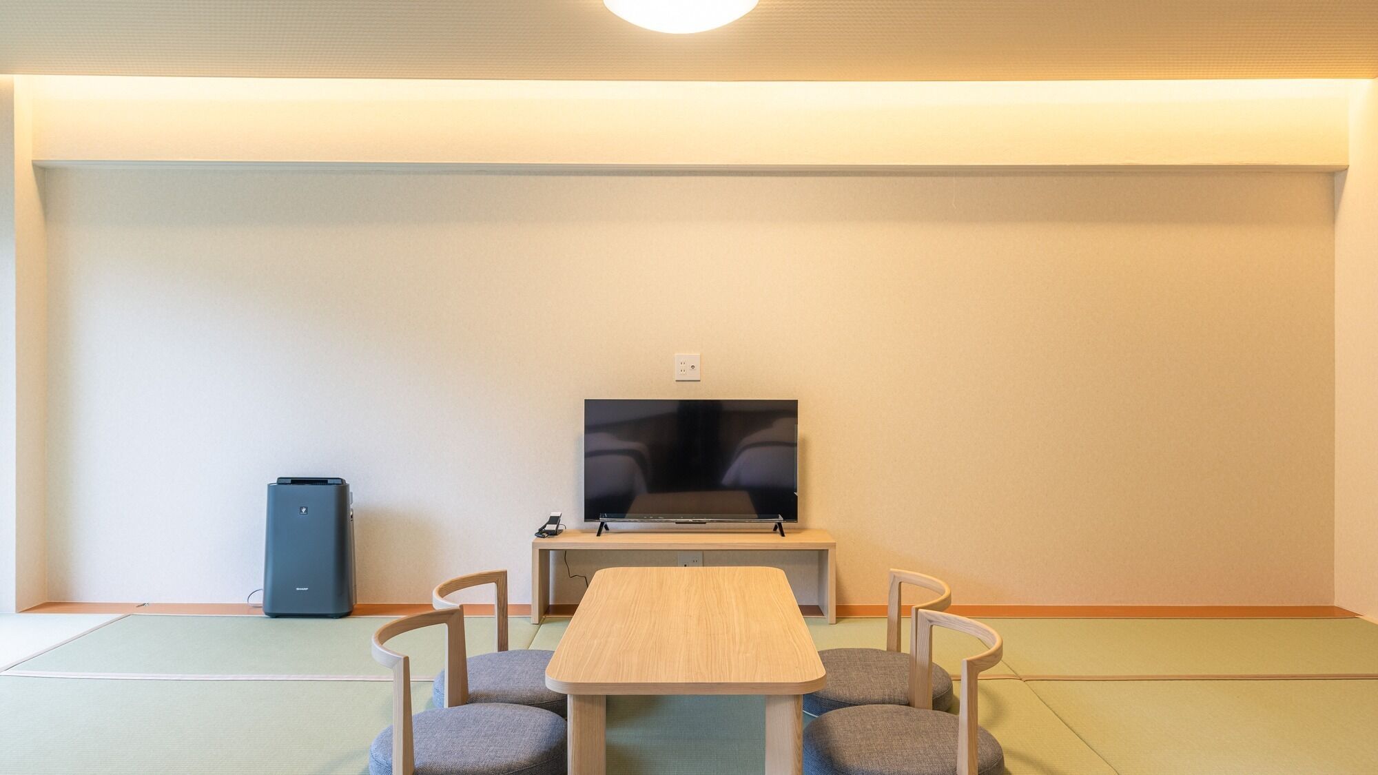 A room with tatami flooring, a wooden table, four chairs, a television, and a small cabinet.