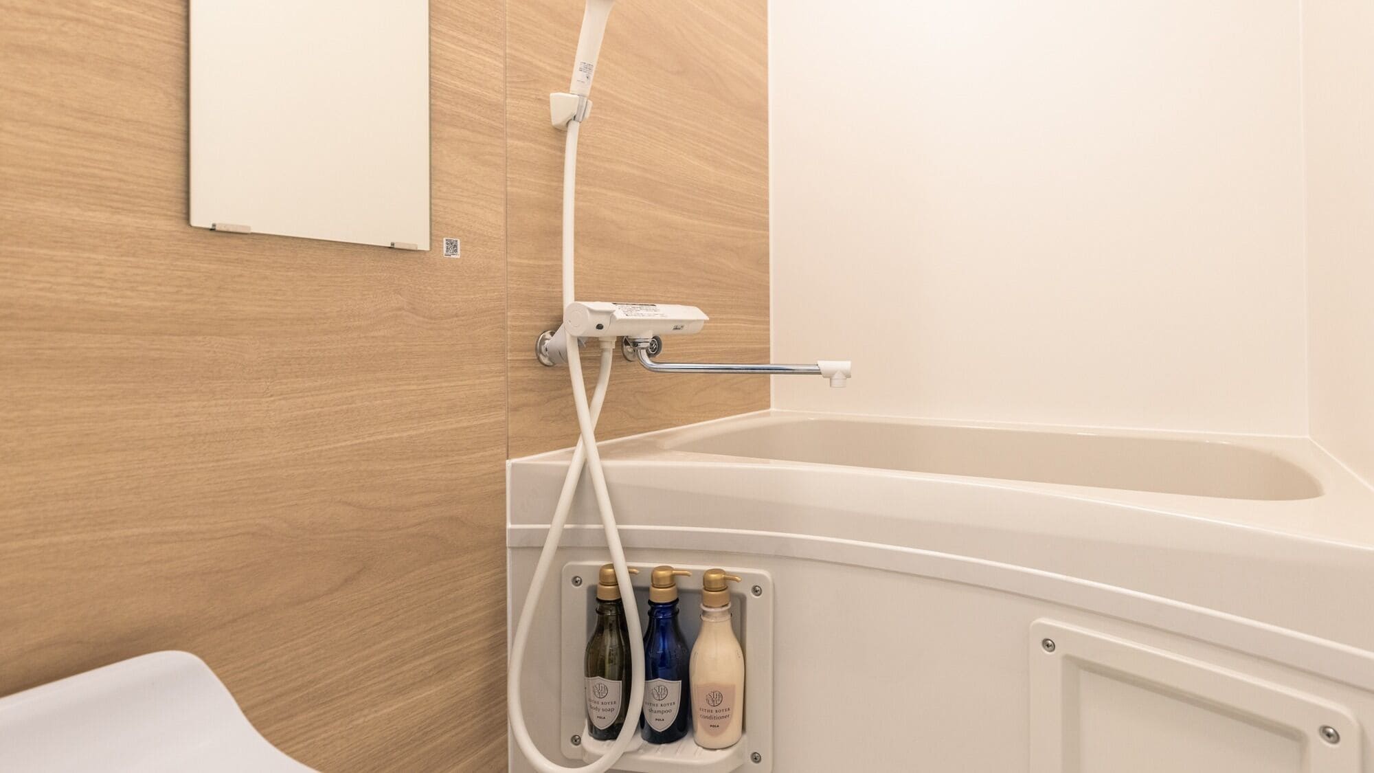 A bathroom with a wooden wall, a white bathtub, and a shelf with three bottles of toiletries.