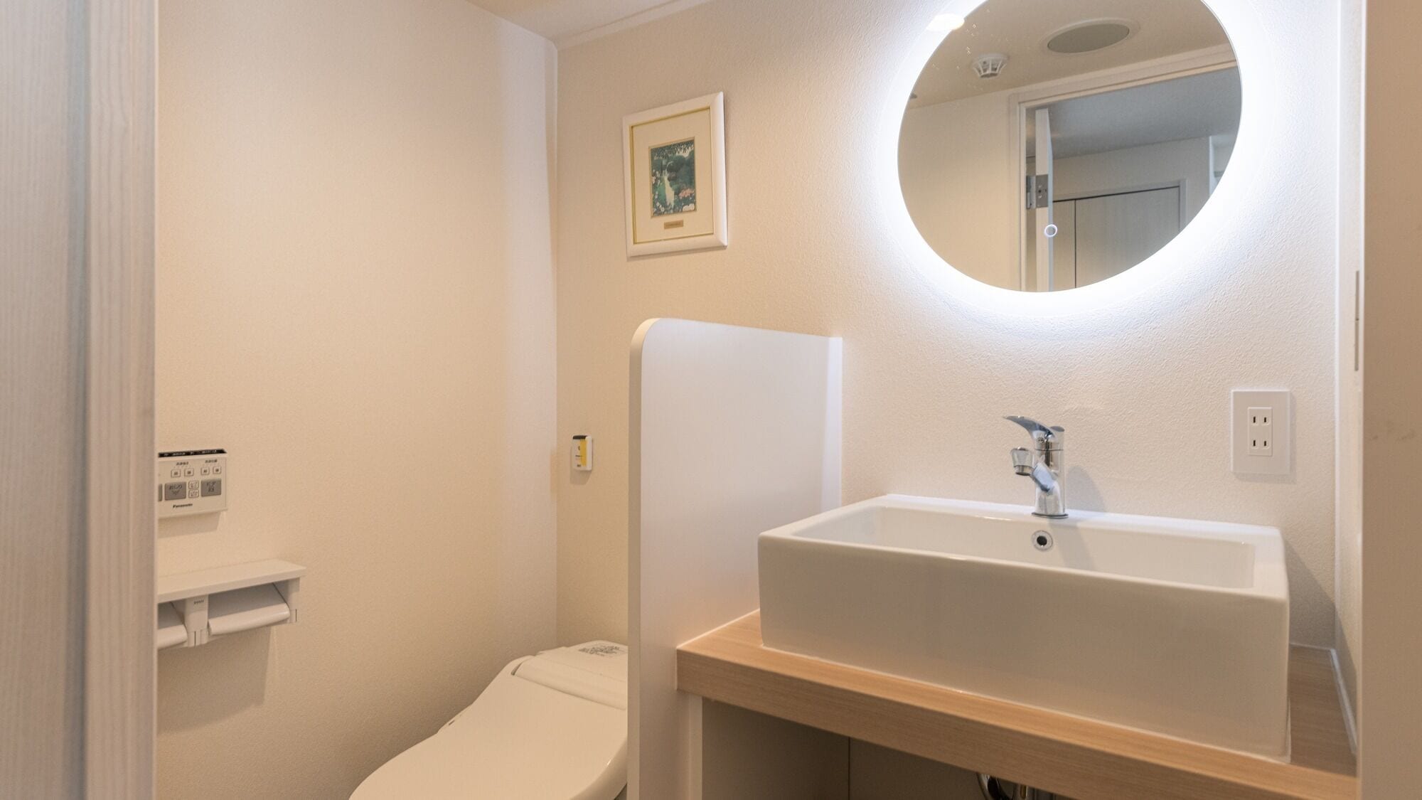 Ein Badezimmer mit weißem Waschbecken, Toilette, wandmontiertem Spiegel und einem kleinen Bild in einem Rahmen.
