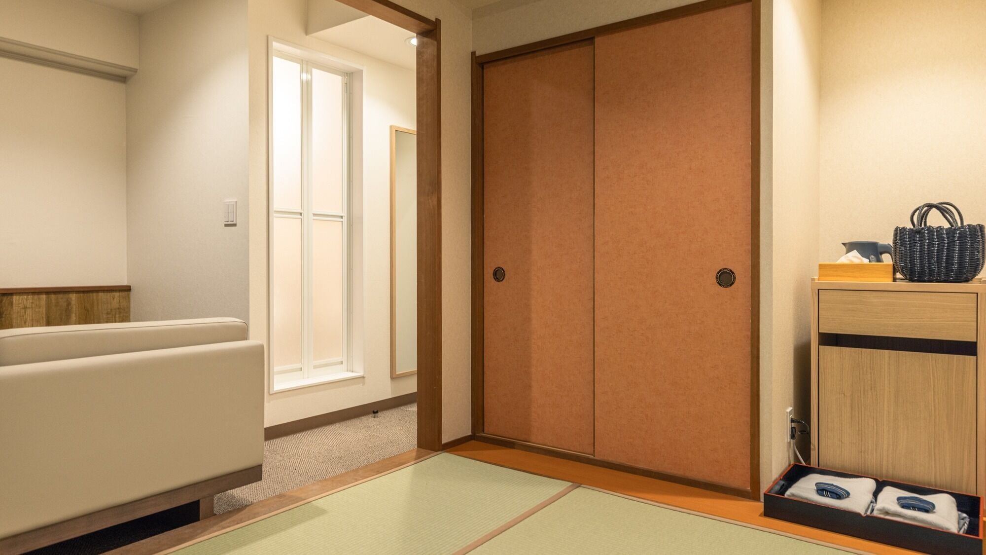 Ein Zimmer mit Schiebetür, einer Couch, einem kleinen Tisch mit einer Tasche und einer Handtuchauslage.
