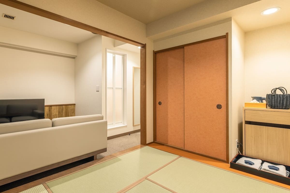 Une chambre d’hôtel équipée d’un canapé, d’une télévision, d’une porte coulissante et d’une petite table d’appoint en bois avec un panier.