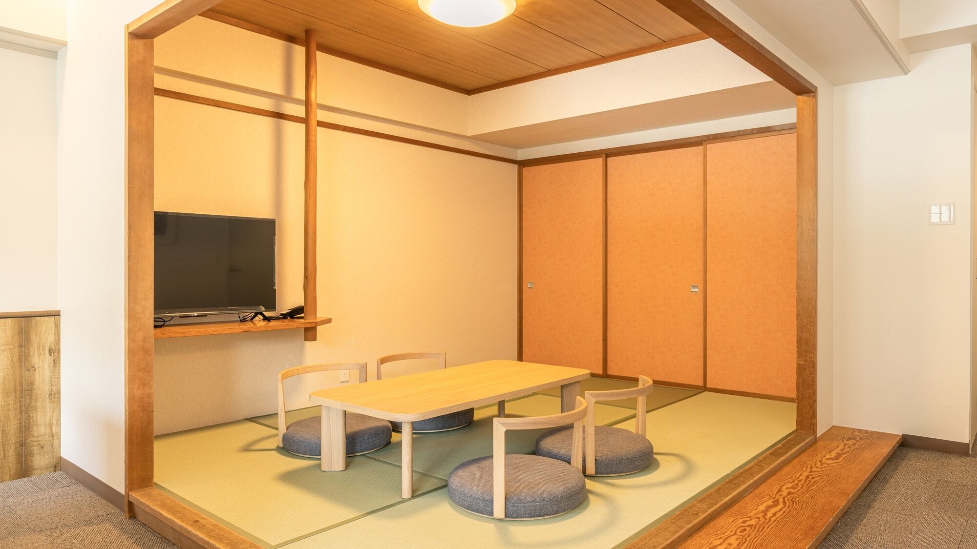 A traditional Japanese-style room with tatami flooring, a low wooden table, and a television on a shelf.