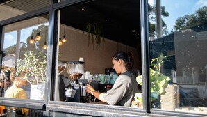 A coffee shop with a large window, a coffee machine, and a person preparing a drink. - The Lookout – Modern Fremantle Apartment with View (Fremantle)