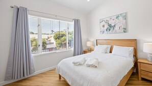 A bedroom with a large bed, a nightstand, a window with curtains, and a wall-mounted painting. - The Lookout – Modern Fremantle Apartment with View (Fremantle)
