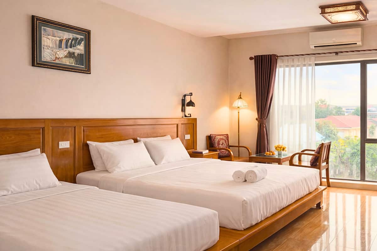 Habitación de hotel con dos camas, una mesita de noche con lámpara, una silla, un ventanal con cortinas y un equipo de aire acondicionado.