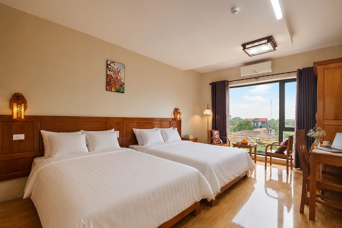 Habitación de hotel con dos camas, un escritorio, una silla, un ventanal con vistas y un equipo de aire acondicionado.