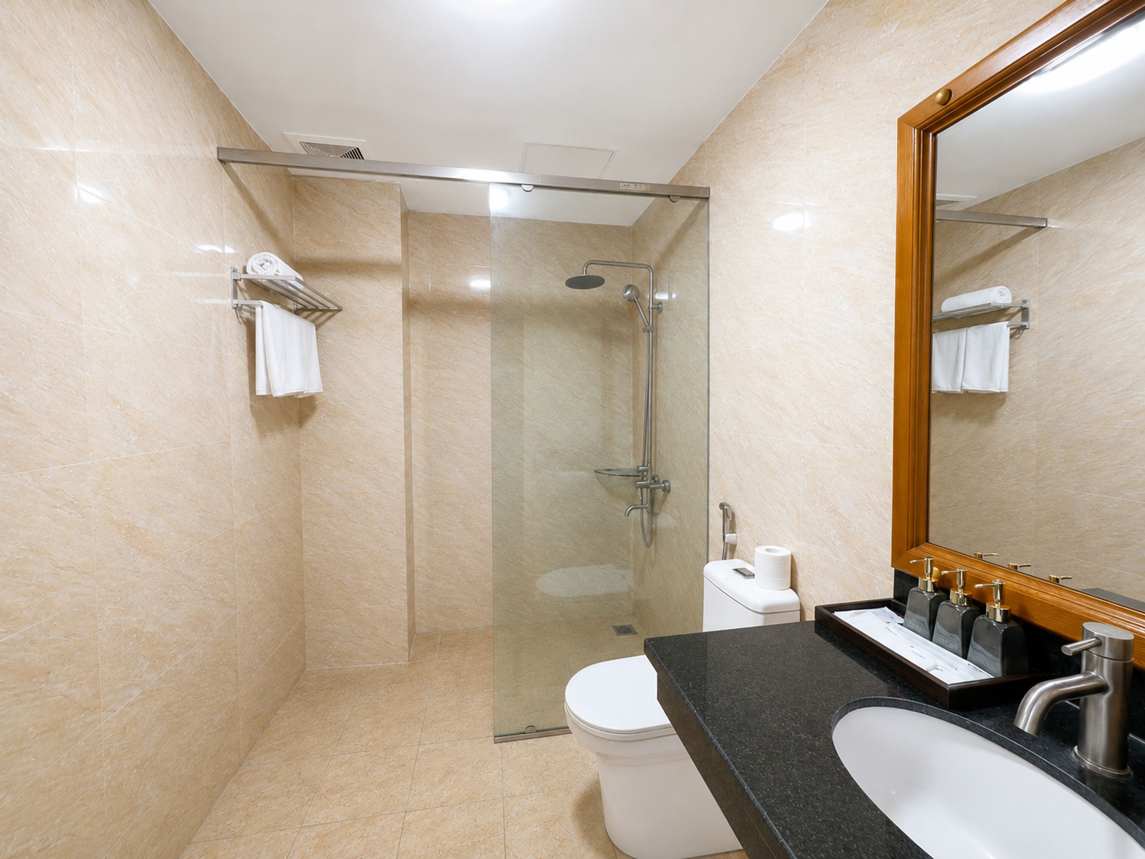 A modern bathroom with a glass-enclosed shower, a white toilet, a black countertop, and a large mirror.