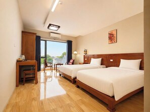 A hotel room with two beds, a desk, a chair, a lamp, and a view of the outdoors. - The Stork House - Serene Garden Retreat (Ninh Binh)
