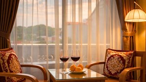 Une chambre d’hôtel avec un balcon, deux chaises, une table avec des verres à vin et des oranges, et une lampe.