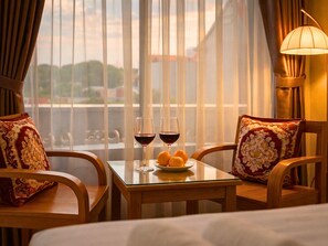 A hotel room with a balcony, two chairs, a table with wine glasses and oranges, and a lamp.