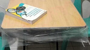 A table with a book and magnifying glasses, covered with plastic, in a room with green chairs.
