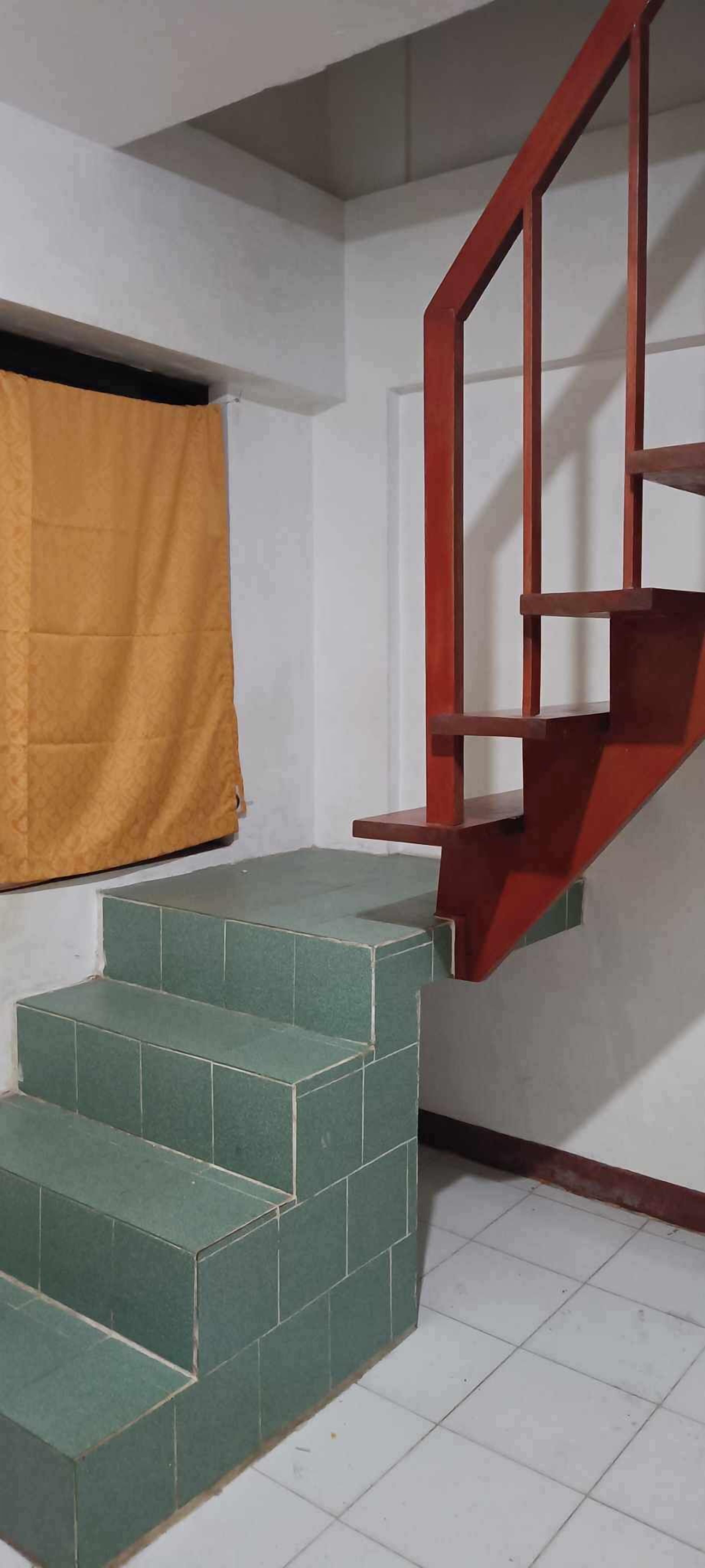 Una escalera con escalones verdes que conduce a una plataforma, un pasamanos rojo y una cortina amarilla en la pared.